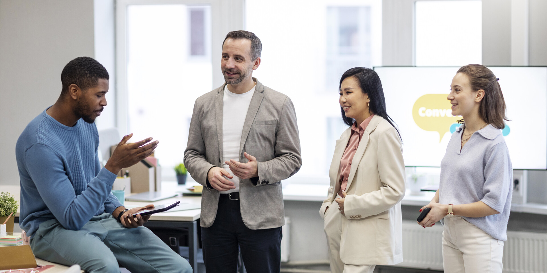Quatre collègues en réunion informelle discutant d’un projet dans un bureau moderne, illustrant la collaboration et la communication interne en entreprise.