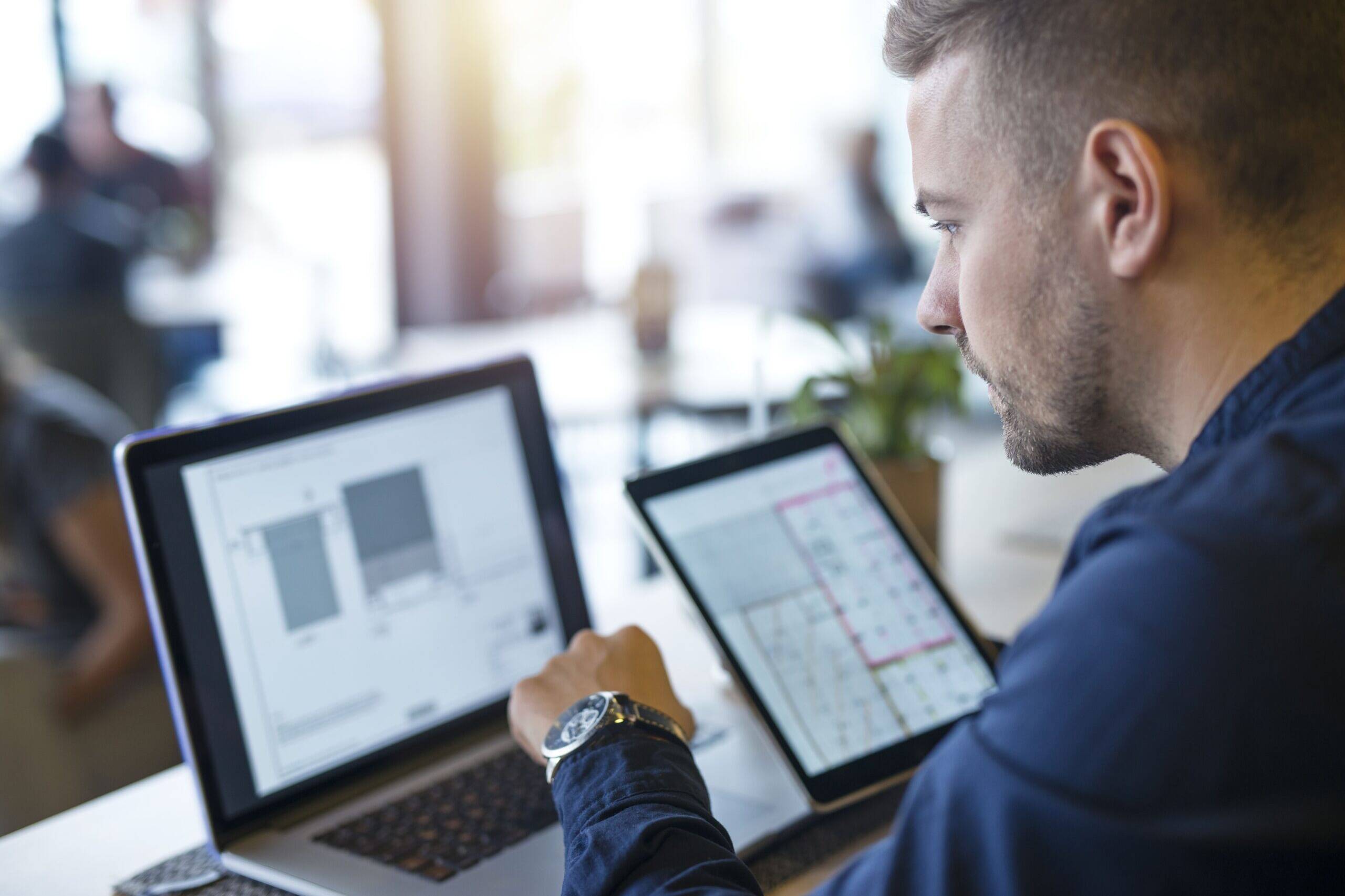 Professionnel analysant des données sur un ordinateur et une tablette dans le cadre d’un projet de transformation numérique.